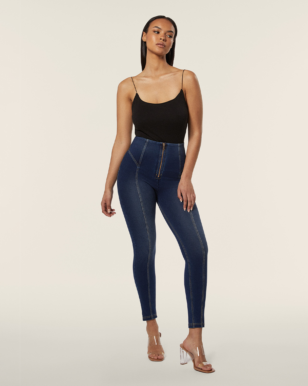 A female model wearing high rise ankle length dark denim rinse pants with a shaping effect and a zipper to fasten, made from organic cotton and recycled elastane.